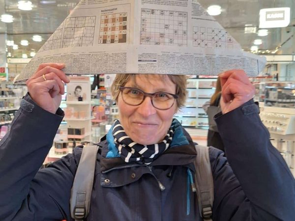Das Bild zeigt eine Frau die eine Zeitung, gefaltet zu einem Hut, über sich hält